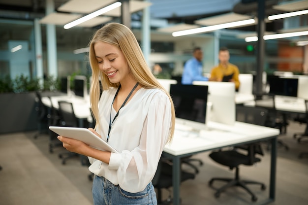 Smiling female manager holds laptop, IT office interior on background. Professional worker, planning or brainstorming. Successful employee in modern company