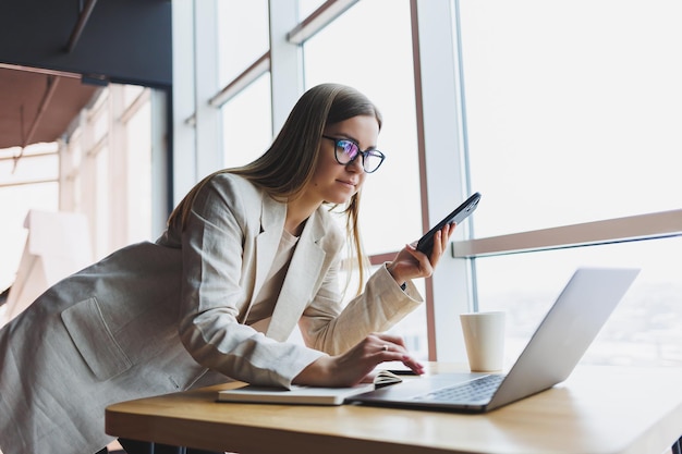 Manager femminile sorridente che utilizza il gadget digitale del telefono cellulare per lavorare tramite l'applicazione online che si connette alla rete wireless 4g in un bar allegro freelance