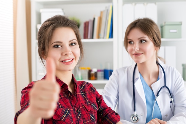 Photo smiling female patient showing ok sign with thumb up at medical doctor office. high level and quality medical service concept. best treatment and patient care concept