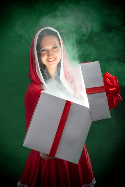濃い緑色の背景に魔法のクリスマス プレゼント ボックスを開く笑顔の女性サンタ
