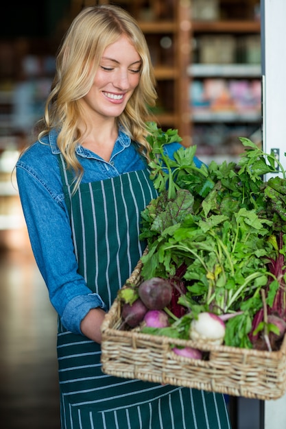 Smiling female staff holding a basket of fresh vegetables