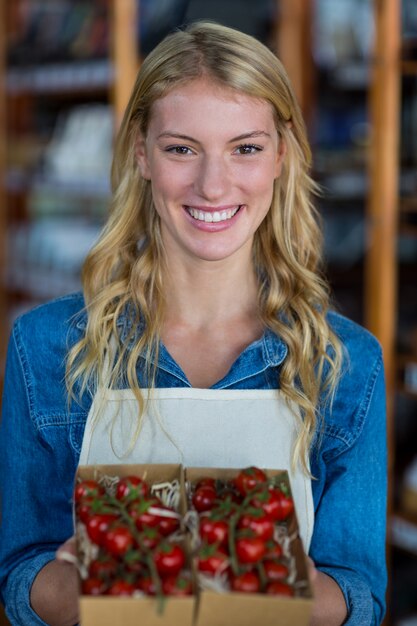 Smiling female staff holding box of cherry tomato in supermarket