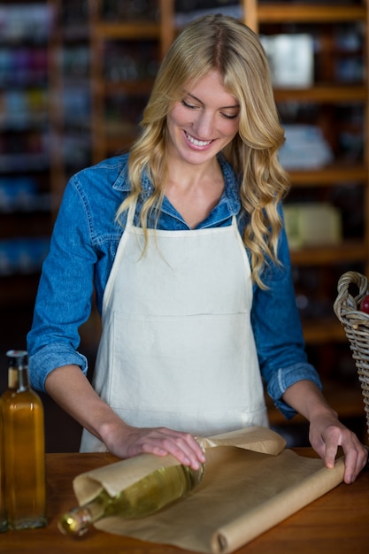 Photo smiling female staff wrapping olive oil bottle with brown paper