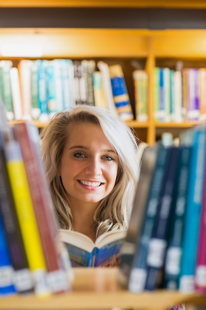 Smiling female student reading book in the library