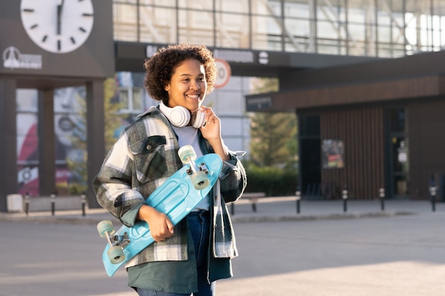 Smiling female teenager holding blue skateboard