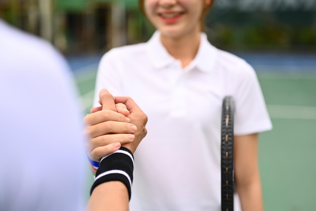 Smiling female tennis players shaking hands with competitor over net at tennis court after the match