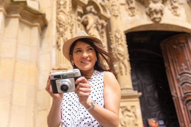 Smiling female tourist in hat visiting a church and taking photos with a camera enjoying spring or summer vacation concept of female traveler and digital content creator