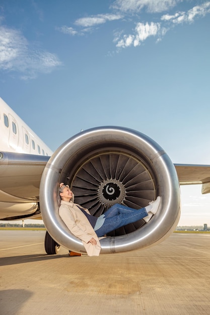 공항에서 푸른 하늘 아래 항공기 터빈 엔진에서 쉬고 웃는 여성 여행자