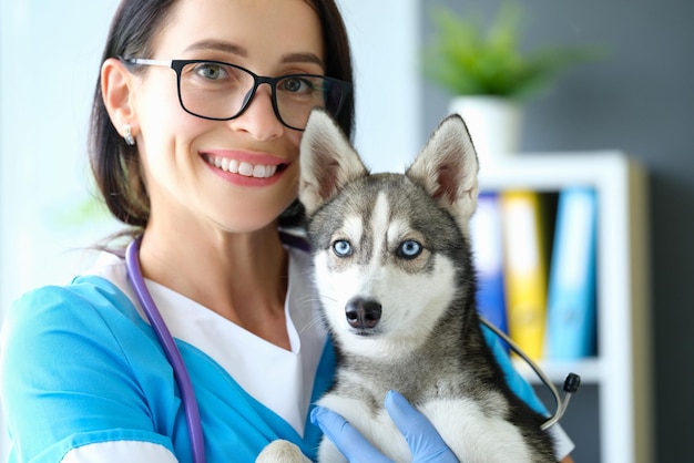 Улыбающаяся женщина-ветеринар держит собаку на руках в клинике
