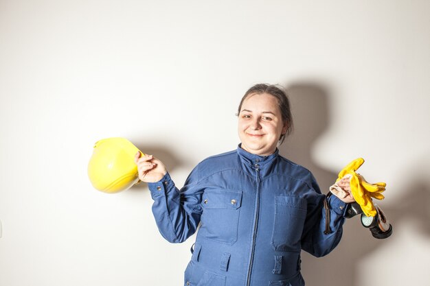 Lavoratrice sorridente vestita con abiti da lavoro, con in mano un casco giallo e guanti gialli