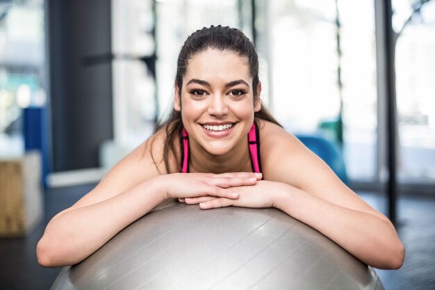 Donna adatta sorridente che si appoggia palla in palestra