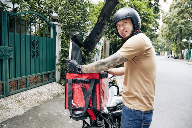 Smiling food delivery service worker taking order out of insulated bag and looking at camera