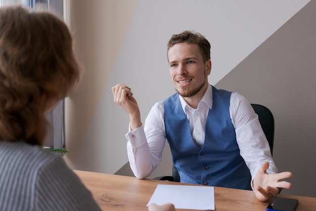 Smiling friendly businessman sees negotiations sitting at office desk holding