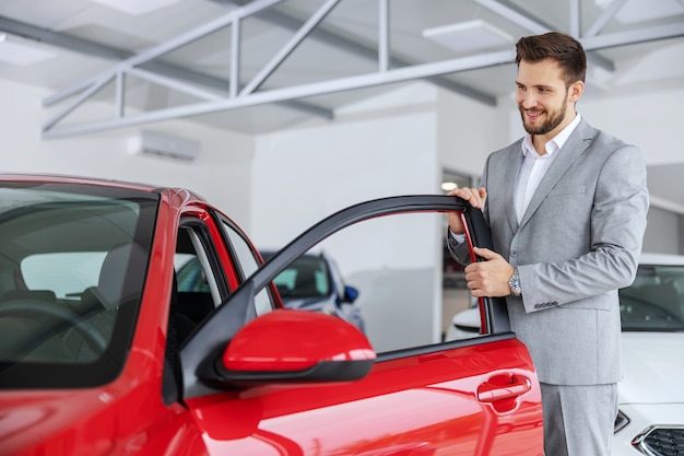 Smiling friendly car seller opening door on a new model of car