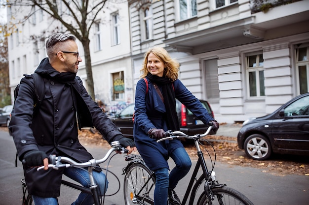 smiling friends cycling on city street in winter