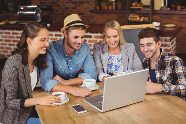 Smiling friends drinking coffee and using laptop