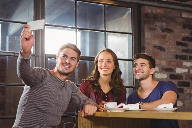 Smiling friends having coffee and taking selfies