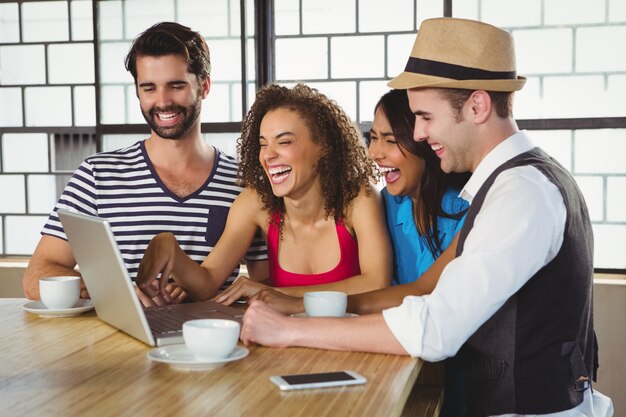 Smiling friends looking at laptop and having coffee