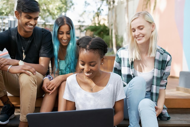 smiling friends looking at laptop outdoors
