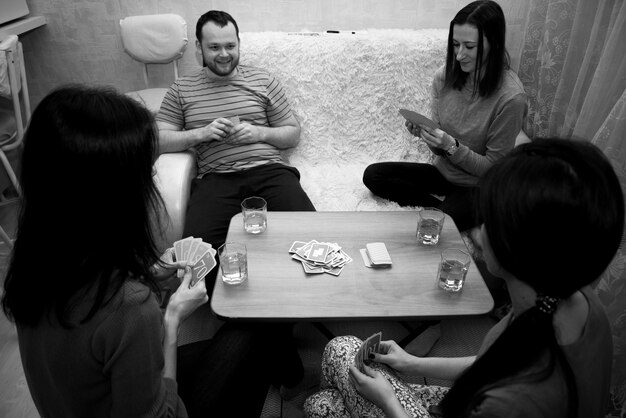 Smiling friends playing cards while sitting on table at home