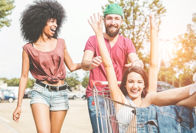 Photo smiling friends pushing woman in shopping cart