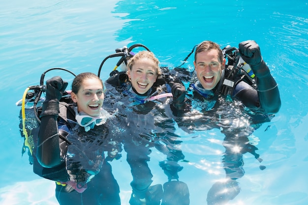 Smiling friends on scuba training in swimming pool cheering at camera