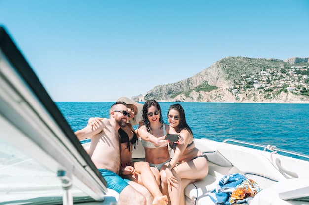 smiling friends sitting on yacht deck taking a selfie with a smartphone