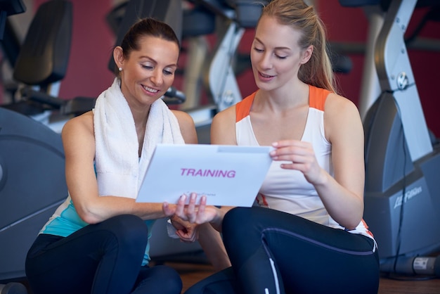 Photo smiling friends using digital tablet while standing at gym