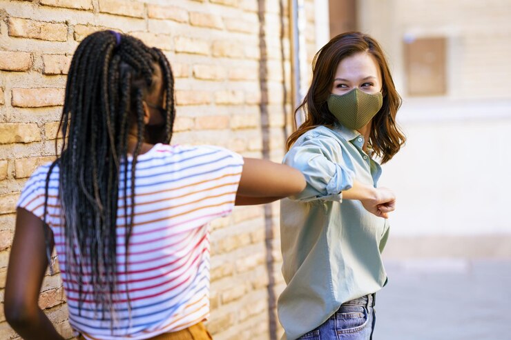 Photo smiling friends wearing mask doing elbow bump against wall