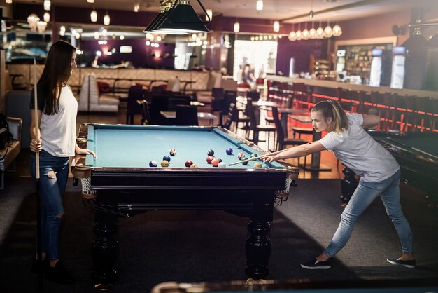 Smiling friends with cues playing billiard in pub