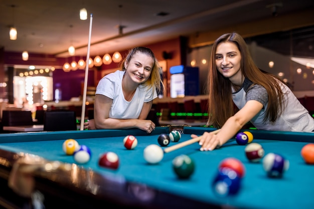 Smiling friends with cues playing billiard in pub