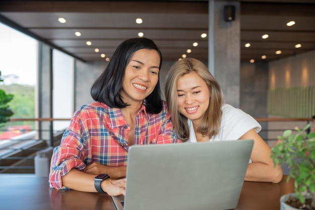 Smiling friends with hot drink using laptop in cafe