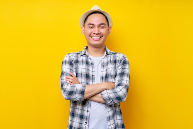 Smiling fun happy smart Young handsome ethnic Asian man 20s wearing casual clothes hat holding hands crossed folded looking at the camera isolated on yellow background People lifestyle concept