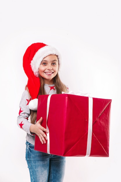 Smiling funny child in Santa red hat holding Christmas gift in hand. Christmas concept.