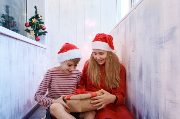 Smiling funny two children in Santa red hat holding Christmas gift in hand.