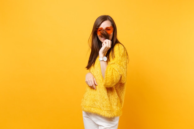 Фото Улыбается забавная молодая женщина в меховом свитере и сердце оранжевые очки, закрывая лицо волосами, изолированными на ярко-желтом фоне. люди искренние эмоции, концепция образа жизни. рекламная площадка.