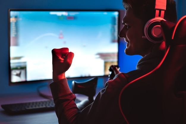 Улыбающийся геймер в наушниках играет в видеоигры на своем персональном компьютере