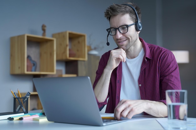 Smiling German guy sitting at home in wireless headset and taking part in online meeting