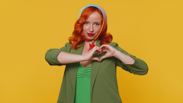 Smiling ginger girl makes heart gesture demonstrates love sign expresses good feelings and sympathy