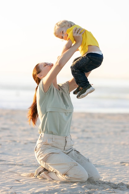 Smiling ginger woman raising up her little son sitting on the beach