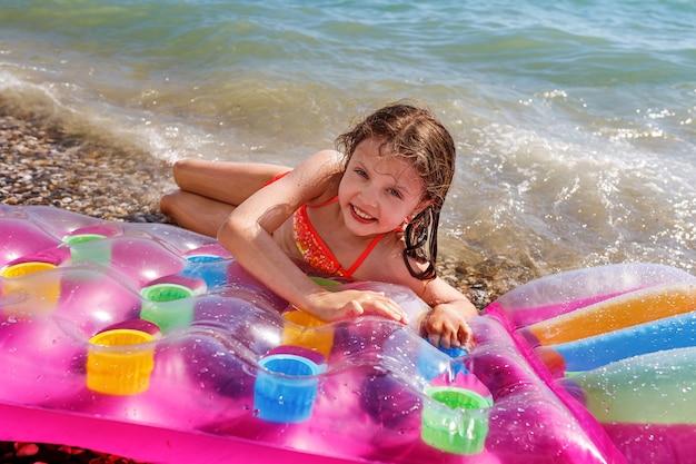 La ragazza sorridente sulla spiaggia in estate su un materasso ad aria sulla spiaggia esamina la macchina fotografica. concetto di intrattenimento estivo