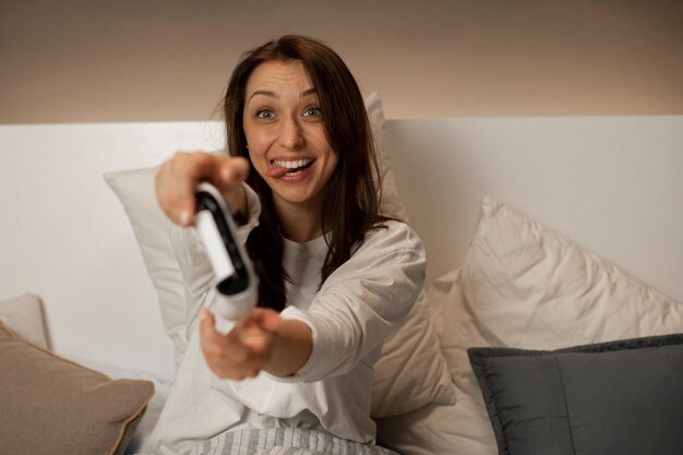 Foto la ragazza sorridente a letto gioca sulla console e tiene il joystick tra le mani