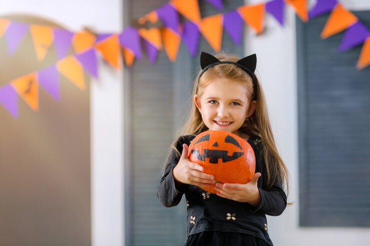 Photo a smiling girl in a carnival costume of a little cat plays with pumpkin and sweets in the room
