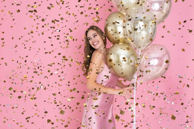 Smiling girl celebrates new year or happy birthday party with confetti while holds many air balloons