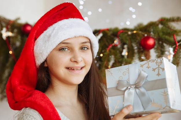 A smiling girl in a christmas hat holds a gift box in her hands