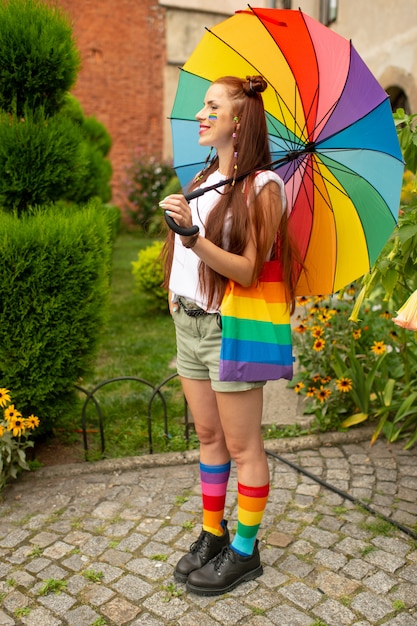 Улыбающаяся девушка в красочной одежде и флаг ЛГБТ на ее позирует на открытом воздухе.