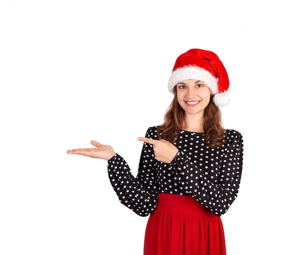 La ragazza sorridente in vestito mostra il dito. ragazza emozionale in cappello di natale di babbo natale isolato su bianco. vacanza