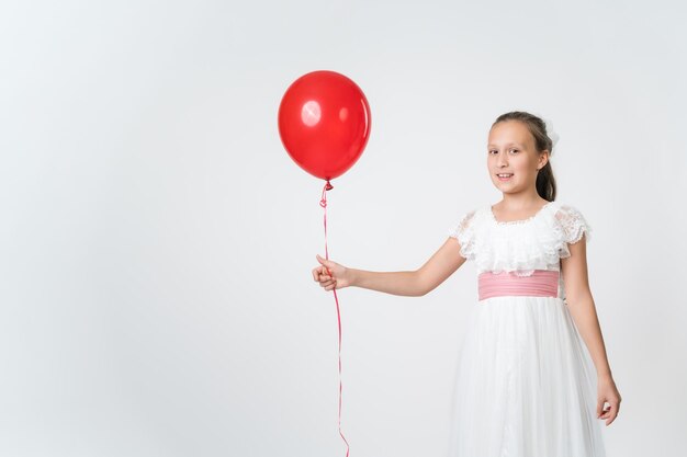 Smiling girl dressed long white dress holding one red balloons in hand smiling looking at camera