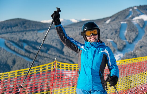 雪に覆われた山の上に立ってスキー休暇を楽しんでいる笑顔の女の子