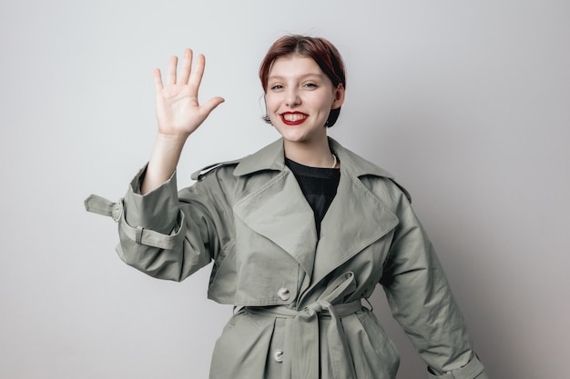 Smiling girl in a fashionable green coat shows the palm of her hand